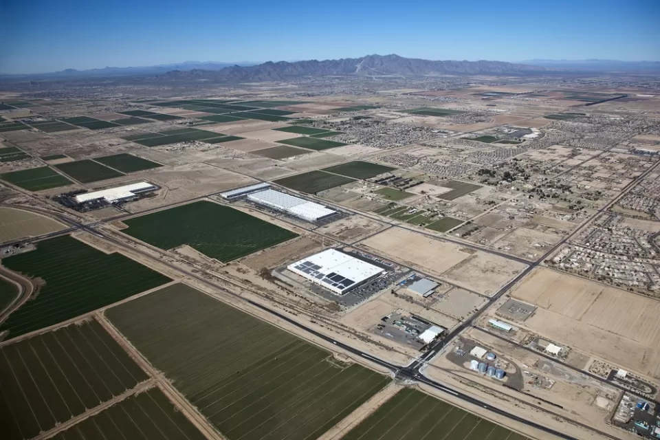 Sprawling warehouses and agricultural landscapes mix with low-rise residential developments in the Arizona desert.